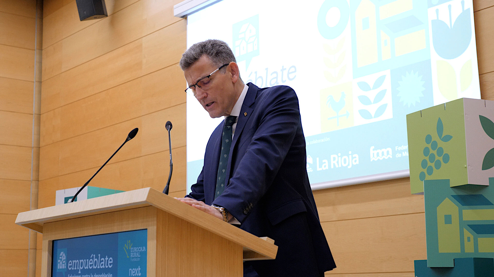 Intervención Víctor Manuel Martín López, Director General de Fundación Eurocaja Rural Intervención desde un atril durante el acto oficial del evento ‘Empuéblate La Rioja’. En el fondo se proyecta una pantalla con elementos gráficos en tonos verdes relacionados con el entorno rural, junto a los logotipos de las entidades organizadoras y colaboradoras.